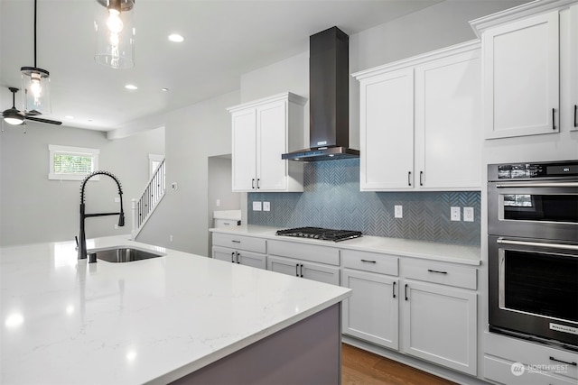 kitchen featuring white cabinetry, sink, stainless steel appliances, wall chimney range hood, and decorative light fixtures