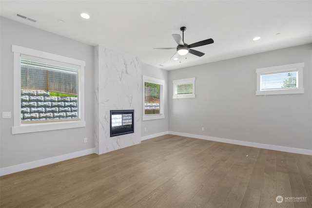 unfurnished living room featuring a high end fireplace, hardwood / wood-style floors, and ceiling fan