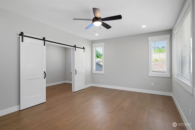 unfurnished bedroom with hardwood / wood-style floors, a barn door, and ceiling fan