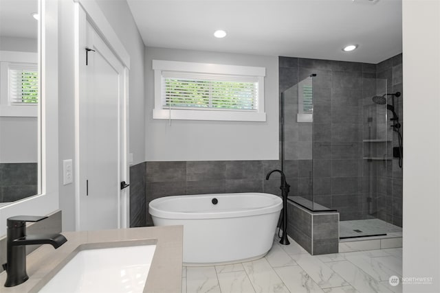 bathroom featuring plus walk in shower, vanity, and tile walls