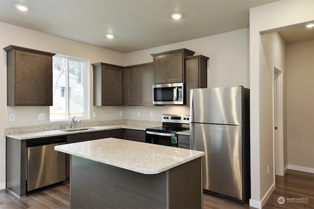 kitchen featuring appliances with stainless steel finishes, light stone counters, dark wood-type flooring, sink, and a kitchen island