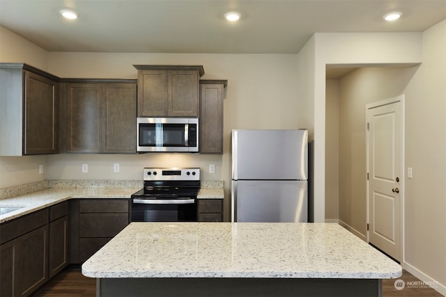 kitchen with light stone counters, a center island, dark wood-type flooring, and appliances with stainless steel finishes