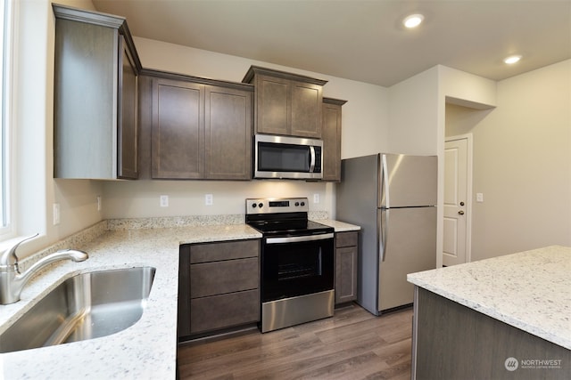 kitchen featuring light stone countertops, appliances with stainless steel finishes, dark hardwood / wood-style flooring, dark brown cabinets, and sink