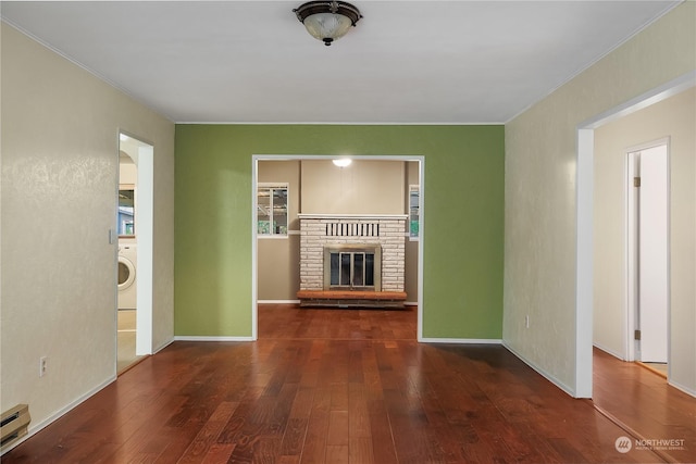 unfurnished living room with a brick fireplace, baseboard heating, dark hardwood / wood-style floors, washer / dryer, and ornamental molding