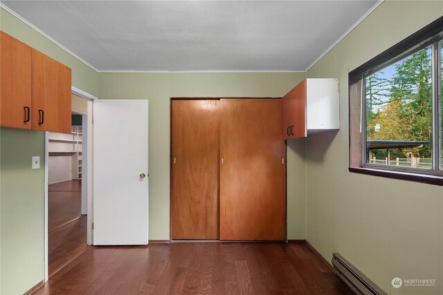 unfurnished bedroom with dark hardwood / wood-style floors, crown molding, a baseboard radiator, and a closet