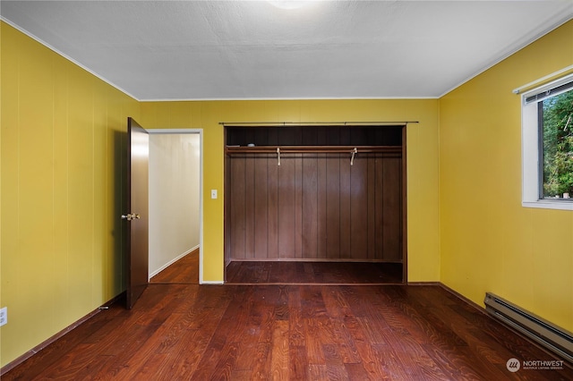 unfurnished bedroom featuring baseboard heating, a closet, and dark wood-type flooring