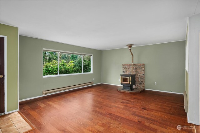 unfurnished living room featuring wood-type flooring, a wood stove, and baseboard heating