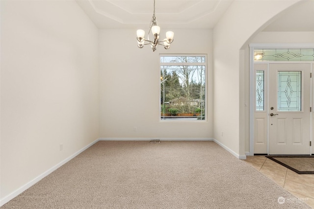 carpeted foyer entrance featuring a raised ceiling and a notable chandelier