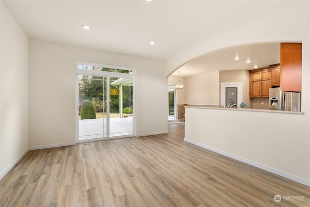 unfurnished living room with a notable chandelier and light hardwood / wood-style flooring