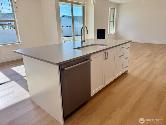 kitchen with white cabinetry, a sink, light wood finished floors, and stainless steel dishwasher