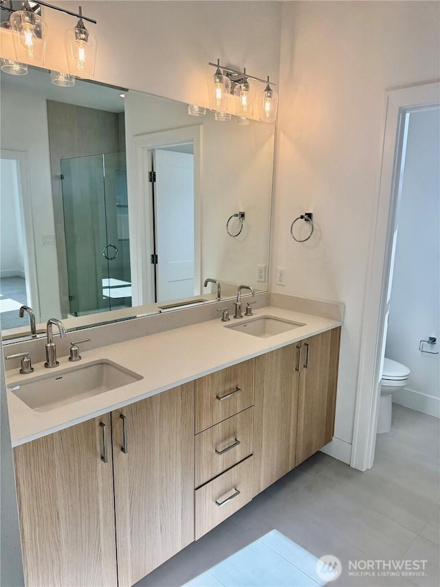 bathroom featuring toilet, a shower stall, double vanity, and a sink