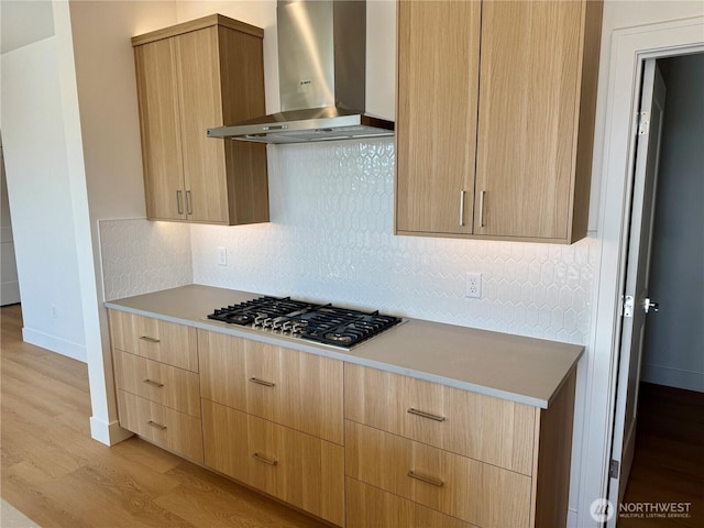 kitchen featuring light brown cabinets, wall chimney exhaust hood, light wood-type flooring, stainless steel gas stovetop, and backsplash