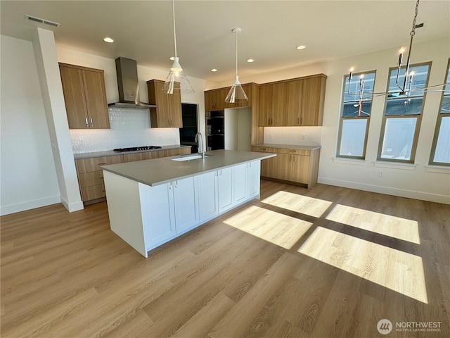 kitchen featuring light wood finished floors, visible vents, wall chimney exhaust hood, gas stovetop, and a sink