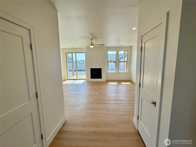 unfurnished living room featuring light wood-type flooring, a fireplace, a ceiling fan, and baseboards