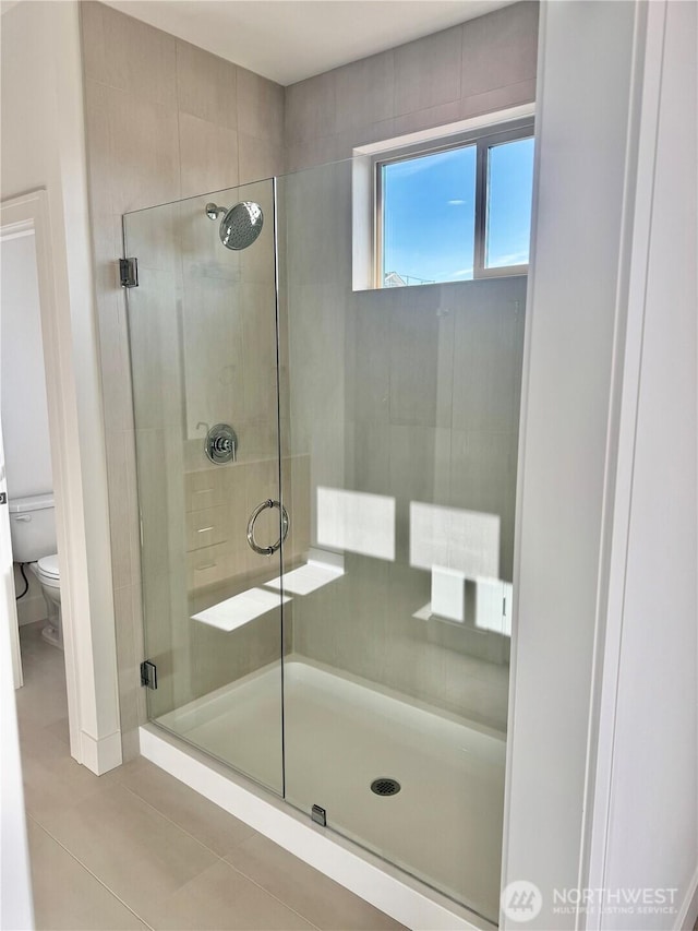 bathroom featuring tile patterned flooring, a shower stall, and toilet