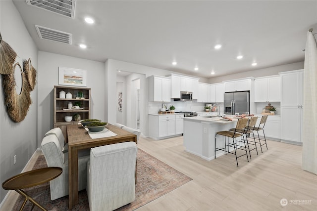 kitchen featuring white cabinets, light wood-type flooring, an island with sink, a kitchen bar, and stainless steel appliances