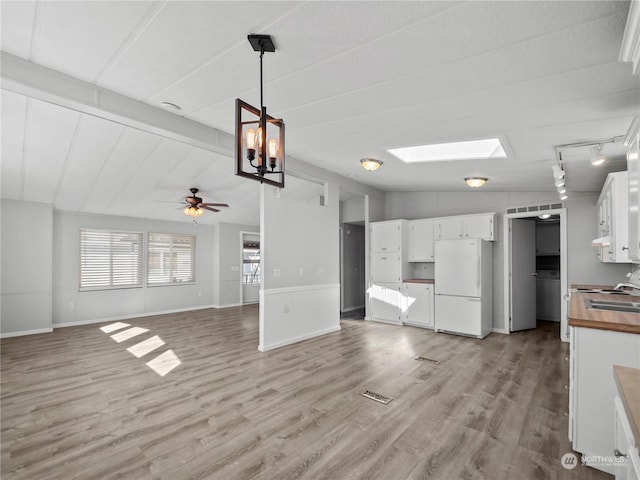 unfurnished living room with track lighting, sink, vaulted ceiling with skylight, ceiling fan, and light hardwood / wood-style floors