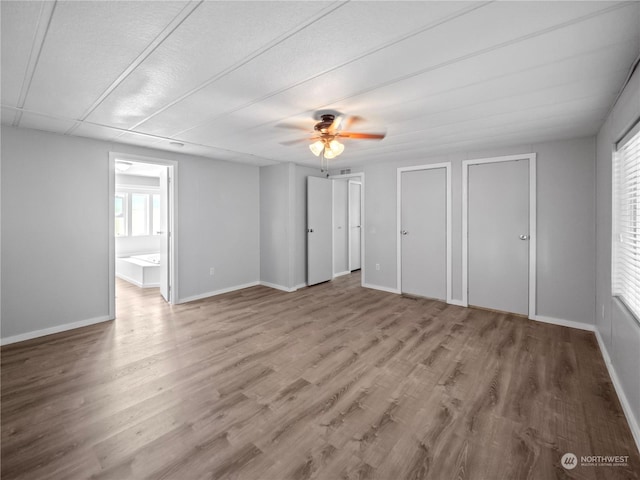 unfurnished bedroom with hardwood / wood-style flooring, ceiling fan, ensuite bathroom, and multiple closets