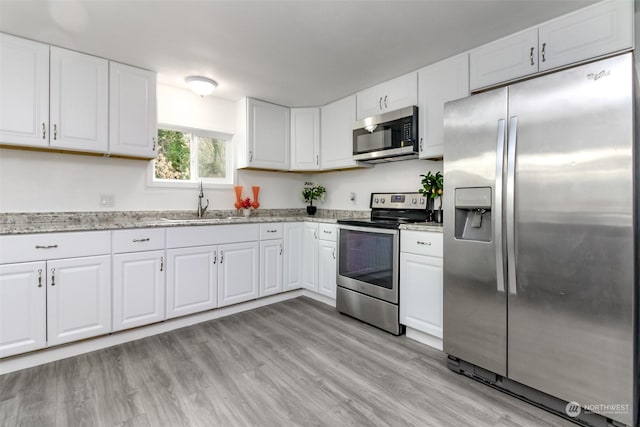 kitchen featuring light stone countertops, light wood-type flooring, stainless steel appliances, sink, and white cabinetry