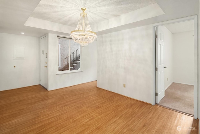 spare room featuring an inviting chandelier, hardwood / wood-style flooring, a raised ceiling, and a textured ceiling