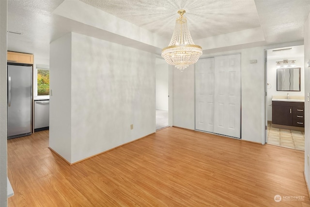 spare room featuring sink, an inviting chandelier, light hardwood / wood-style flooring, a textured ceiling, and a tray ceiling