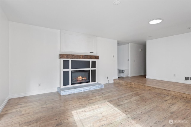 unfurnished living room with light wood-type flooring and a brick fireplace