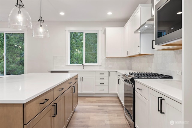 kitchen with stainless steel appliances, light countertops, wall chimney range hood, white cabinetry, and pendant lighting