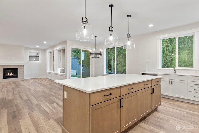 kitchen with a sink, open floor plan, light countertops, hanging light fixtures, and light brown cabinetry