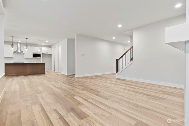 unfurnished living room featuring stairs, recessed lighting, baseboards, and light wood-style floors