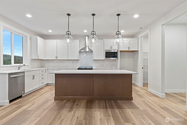 kitchen with a center island, light countertops, appliances with stainless steel finishes, white cabinetry, and wall chimney range hood