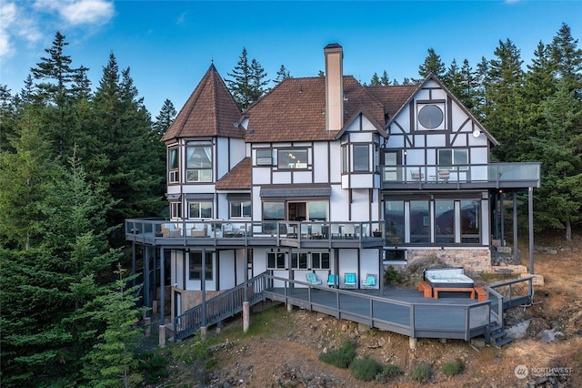 back of property with a balcony, a wooden deck, and a hot tub