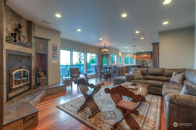 living room featuring a chandelier, ornamental molding, a fireplace, and light hardwood / wood-style flooring