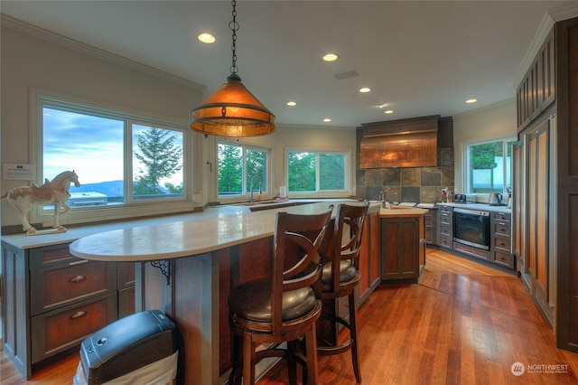 kitchen with backsplash, crown molding, hardwood / wood-style floors, pendant lighting, and a kitchen island with sink