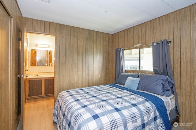 bedroom featuring sink, light wood-type flooring, ensuite bathroom, and wood walls