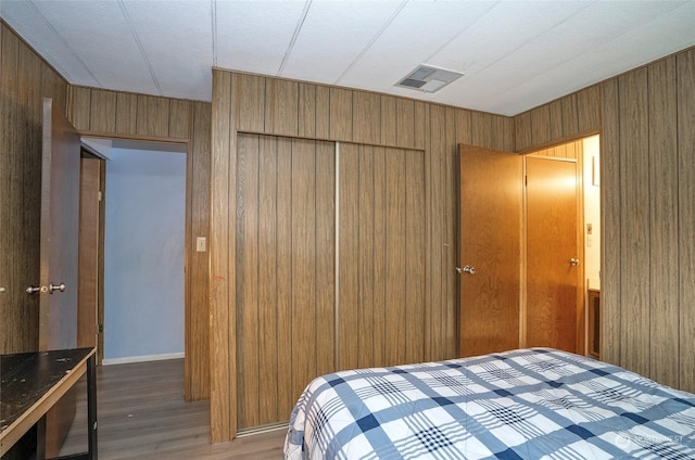 bedroom featuring hardwood / wood-style floors, wooden walls, and a closet