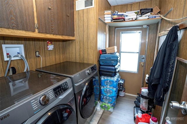 washroom with wooden walls, washer and clothes dryer, cabinets, and wood-type flooring