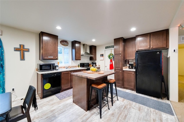 kitchen featuring a center island, wall chimney exhaust hood, black appliances, and light hardwood / wood-style floors