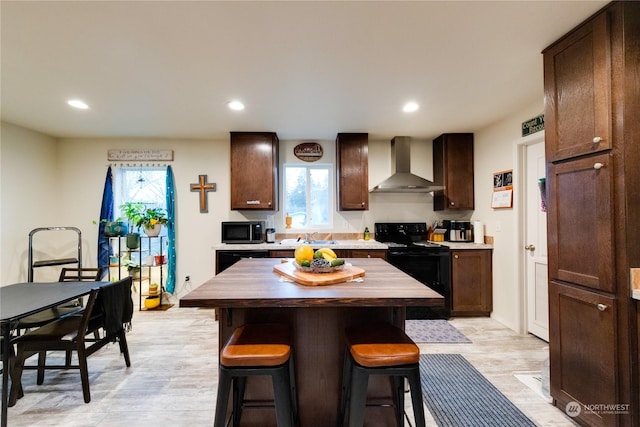 kitchen with plenty of natural light, wall chimney exhaust hood, black appliances, and light wood-type flooring