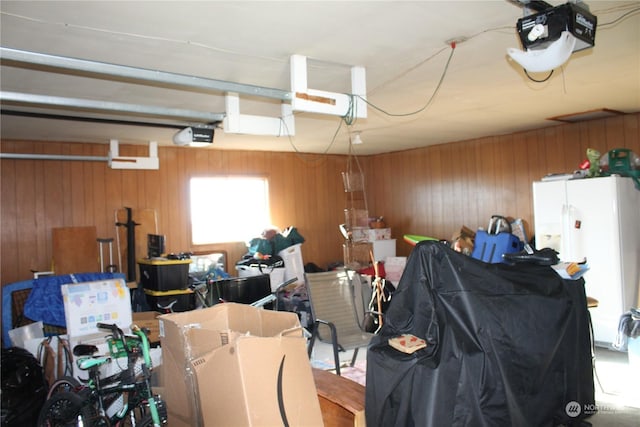 garage featuring wood walls, white fridge with ice dispenser, and a garage door opener