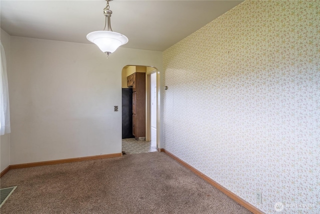 empty room with arched walkways, visible vents, wallpapered walls, and baseboards