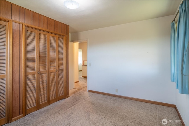 unfurnished bedroom featuring arched walkways, baseboards, a closet, and light colored carpet