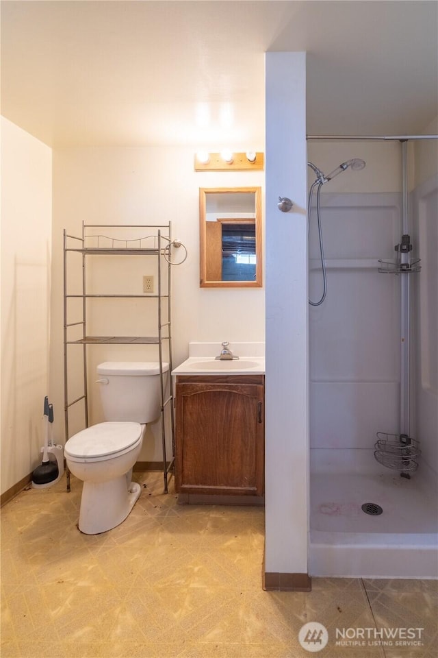 bathroom featuring a shower stall, toilet, vanity, and baseboards