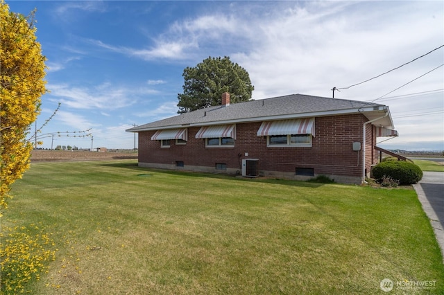 rear view of house with a lawn, a chimney, a shingled roof, cooling unit, and brick siding