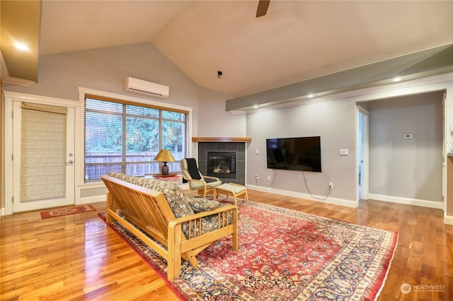 living room with hardwood / wood-style floors, vaulted ceiling, a wall mounted AC, and a tiled fireplace