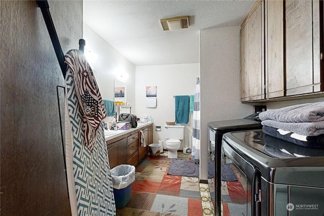 bathroom featuring toilet, washing machine and dryer, a textured ceiling, and vanity