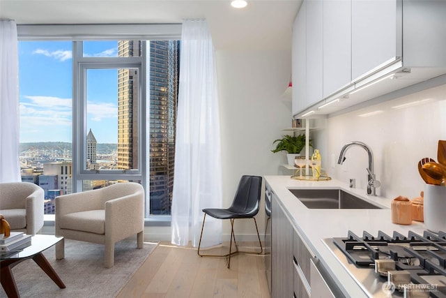 kitchen with stainless steel gas cooktop, a sink, white cabinetry, light countertops, and light wood-type flooring