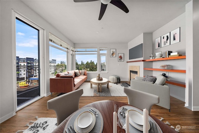 living area featuring a fireplace, wood finished floors, baseboards, and a ceiling fan