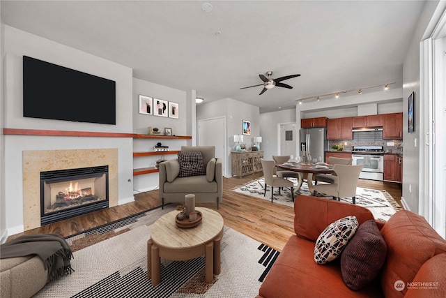 living room with baseboards, a lit fireplace, light wood-style flooring, and a ceiling fan