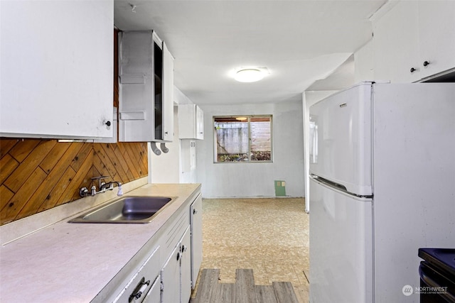 kitchen with white cabinetry, sink, wooden walls, and white refrigerator