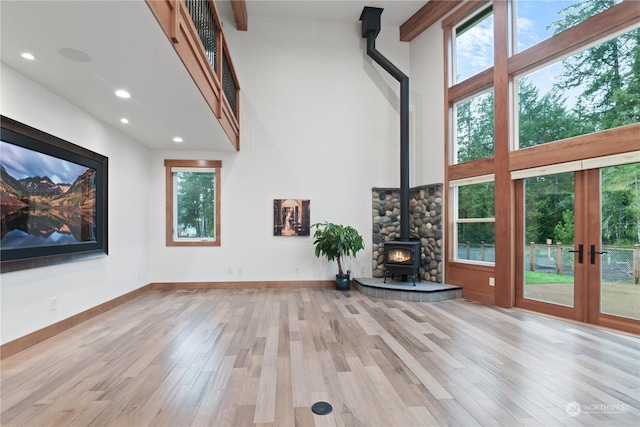 unfurnished living room featuring a towering ceiling, a wood stove, light wood-type flooring, and french doors